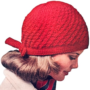 May include: A red knitted hat with a tied bow at the back. The hat has a textured pattern and is worn by a person with blonde hair.