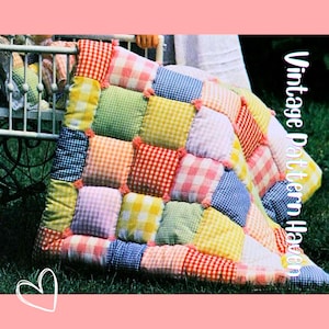 Op de afbeelding: Een kleurrijke patchworkquilt met vierkanten van rood, geel, groen, blauw en roze geruite stof. De quilt ligt op het gras naast een vintage kinderwagen. De tekst "Vintage Pattern Haven" staat aan de rechterkant.