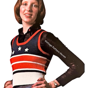 May include: A sleeveless knitted vest with red, white, and blue stripes and stars. The vest has a scoop neck and is cropped. The model is wearing a black long-sleeved shirt underneath the vest.