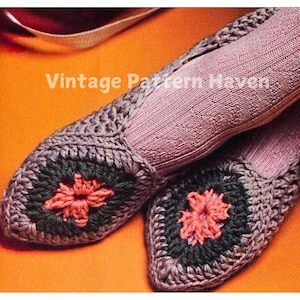 Puede incluir: Un par de zapatillas de crochet con punta puntiaguda y un diseño de flor en el centro. Las zapatillas están hechas con una combinación de hilo morado, gris y rosa.