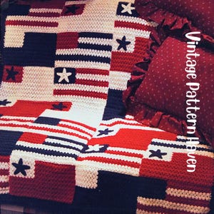 May include: A handmade crochet blanket with a patriotic design. The blanket features red, white, and navy blue squares with star and stripe patterns. The text "Vintage Pattern Haven" is visible on the right side of the image. A red pillow with a ruffled edge is also visible.