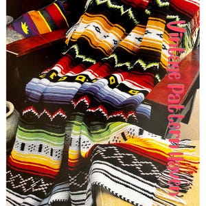 Könnte beinhalten: Eine bunte Häkeldecke mit einem südwestlichen Muster in Rot-, Orange-, Gelb-, Grün-, Blau- und Schwarztönen. Die Decke ist gefaltet und über einen Holzstuhl gelegt. Der Text "Vintage Pattern Haven" ist im Bild sichtbar.