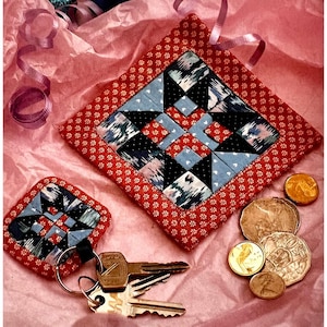 Puede incluir: Dos cuadrados de tela roja con un diseño de patchwork. El cuadrado más grande tiene un borde blanco con pequeñas flores rojas. El cuadrado más pequeño está unido a un llavero con llaves. Ambos cuadrados tienen un patrón geométrico azul, negro y blanco.