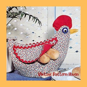 May include: A fabric chicken-shaped bread warmer with a red comb and wattle, blue and white eye, and yellow beak. The body is patterned with small red, blue, and white flowers. The bread warmer holds two rolls. The text "Vintage Pattern Haven" is visible.
