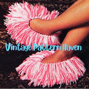 May include: A pair of pink and white crocheted slippers with long fringe. The slippers are worn on a person's feet. The text "Vintage Pattern Haven" is visible in the image.