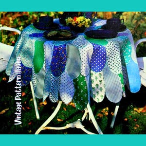 Könnte beinhalten: Ein runder Tisch mit einer bunten Tischdecke. Die Tischdecke hat einen gewellten Rand mit verschiedenen Stoffmustern in Blau, Grün und Weiß. Der Tisch ist mit schwarzen Hüten, Tellern und einer kleinen Blumenvase gedeckt. Der Text "Vintage Pattern Haven" ist sichtbar.