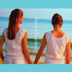 Pode incluir: Dois tops de malha branca sem mangas com um padrão de diamante texturizado e cós canelado. Os tops apresentam um decote redondo e são exibidos em duas pessoas de frente para o oceano. O texto Vintage Pattern Haven é visível.