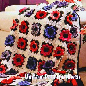 May include: A handmade crochet blanket featuring a floral pattern. The blanket is cream-colored with square motifs, each adorned with red, purple, and blue flower designs. The text "Vintage Pattern Haven" is visible.