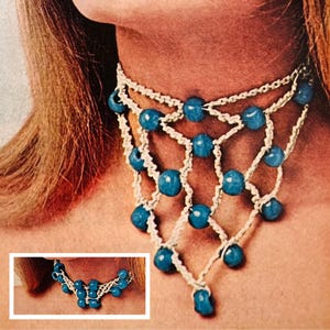 以下が含まれることがあります： 青いビーズと白い糸で編まれたクロシェネックレス。ネックレスは重ねてあり、V字型のデザインになっています。