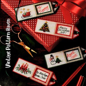 May include: Handmade Christmas gift tags with cross-stitch designs. The tags display festive images such as a Christmas tree, snowman, and sleigh, alongside text that reads "To: Timmy", "Merry Christmas Jeff!", "Aunt Sue", and "To: Marilyn From: Sue".