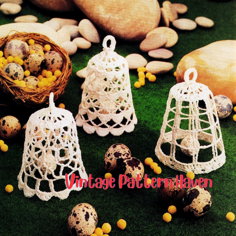 May include: Three white crochet bell ornaments with intricate openwork designs. The bells are displayed with speckled eggs, a woven nest, and small yellow beads on a green surface. The text "Vintage Pattern Haven" is visible.