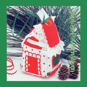 May include: A handmade Christmas ornament shaped like a house. The roof is red, and the walls are white with red polka dots. The house has a red door, green accents, and white lace trim. A green ribbon is attached for hanging.
