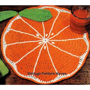 Puede incluir: Patrón de posavasos de crochet en forma de rodaja de naranja. El posavasos está hecho con hilo naranja y blanco y presenta una hoja de crochet verde. El texto "Vintage Pattern Haven" es visible en la parte inferior central de la imagen.