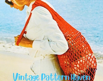 May include: A woman wearing a white shirt and white pants walks on a beach carrying a bright red crocheted net bag with a tassel.