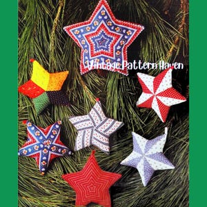 May include: A selection of star-shaped fabric decorations in various colours and patterns. The stars display floral prints, patchwork designs, and solid hues. The ornaments are set against a backdrop of green pine needles, with the text "Vintage Pattern Haven".
