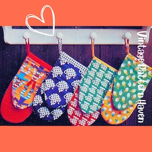 Könnte beinhalten: Fünf bunte Ofenhandschuhe hängen an einem weißen Gestell vor einem dunklen Holzgrund. Die Handschuhe zeigen verschiedene Muster, darunter Schafe und Teetassen, in Rot, Blau, Grün und Gelb. Jeder Handschuh hat eine Schlaufe zum Aufhängen.