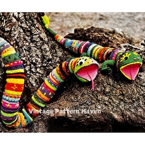 May include: Two colourful knitted snake puppets with open mouths and green heads. The snakes are wrapped around a tree trunk.