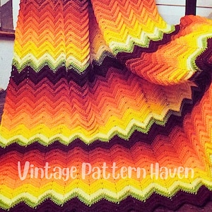 May include: A crocheted blanket with a chevron pattern in shades of orange, yellow, green, and brown. The blanket is folded in half and the text "Vintage Pattern Haven" is visible in the lower center of the image.