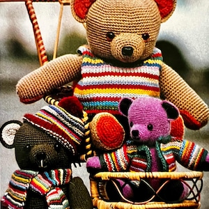 May include: Three handmade crochet teddy bears. The largest bear is tan with a striped sweater. A black bear wears a striped hat and scarf. A purple bear sits in a basket and wears a striped jacket. All bears have black eyes and noses.