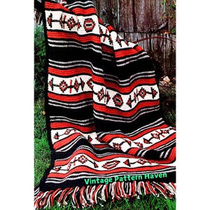 Könnte beinhalten: Eine Häkeldecke mit einem gestreiften Muster in Rot, Schwarz und Weiß. Die Decke hat einen Fransenrand und ein geometrisches Muster.