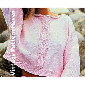 May include: A pink knitted sweater with a cable knit design down the front. The sweater has a boat neck and long sleeves.