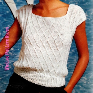 May include: A white knit top featuring a square neckline and short cap sleeves. The garment displays a textured diagonal diamond pattern across the front, with vertical ribbed detailing along the sides and a wide ribbed hem at the waistline.