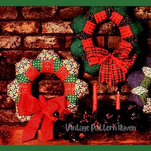 May include: Two fabric wreaths featuring quilted patchwork designs in red, green, and multi-colored patterns. Each wreath is accented with a large red fabric bow. The text Vintage Pattern Haven is visible at the bottom of the image.