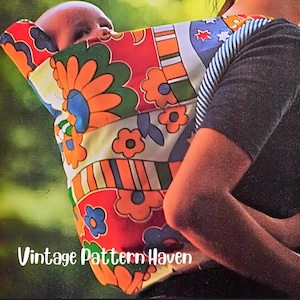 May include: A colorful baby carrier with a retro floral pattern in orange, red, blue, and green. The carrier is being worn by a person with a dark gray long-sleeved shirt. The text "Vintage Pattern Haven" is visible.
