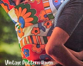 May include: A colorful baby carrier with a retro floral pattern in orange, red, blue, and green. The carrier is being worn by a person with a dark gray long-sleeved shirt. The text "Vintage Pattern Haven" is visible.