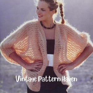 Può includere: Un cardigan rosa chiaro a maglia aperta con una texture soffice. Il cardigan ha una vestibilità rilassata e maniche a tre quarti. La modella indossa il cardigan sopra un top nero senza maniche e una cintura bianca.