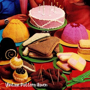 Könnte beinhalten: Eine Sammlung gestrickter Lebensmittel, darunter ein rosa Kuchen mit Kerzen, Sandwiches und Donuts. Die Artikel sind auf Tellern in verschiedenen Farben angeordnet, die auf einer roten Tischdecke stehen. Der Text "Vintage Pattern Haven" ist sichtbar.