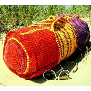 May include: A red, yellow, and purple striped crocheted tote bag with a round bottom. The bag is sitting on a sandy beach with a pair of sunglasses next to it. The text "Vintage Pattern Haven" is printed on the bag.