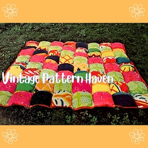 May include: A vibrant patchwork quilt featuring a mix of patterns and colours, such as red, pink, green, yellow, and blue. The quilt is laid out on green grass. The text "Vintage Pattern Haven" is visible on the quilt.