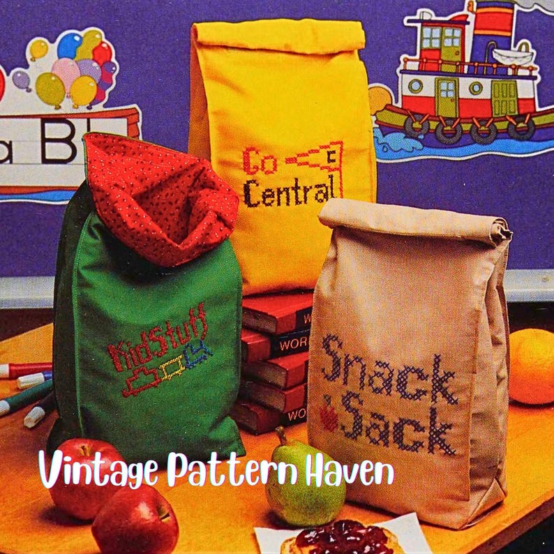 Puede incluir: Tres bolsas de almuerzo de tela en amarillo, verde y beige, cada una bordada con texto. La bolsa amarilla dice "Co-Central", la bolsa verde dice "KidStuff" y la bolsa beige dice "Snack Sack". Manzanas, peras y un peque&ntilde;o refrigerio en primer plano.