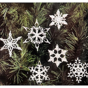 May include: Six white crocheted snowflakes hanging on a green pine tree branch. The snowflakes are different sizes and designs.