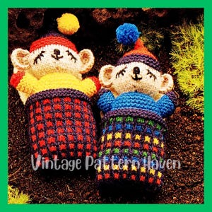 May include: Two handmade knitted bear dolls with red, yellow, and blue accents. Each bear wears a hat with a pom-pom and is seated in a matching basket. The text "Vintage Pattern Haven" is visible.