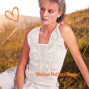 Może przedstawiać: Kobieta w białym, bezrękawnym topie z szydełka z kwadratowym dekoltem. Top ma delikatny, ażurowy wzór. Widoczny jest tekst "Vintage Pattern Haven". Tło to pole wysokiej trawy.