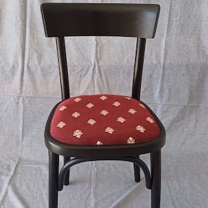 May include: A black wooden chair with a red fabric seat featuring a white floral pattern. The chair has a simple design with a curved back and straight legs.