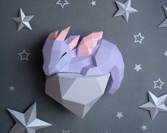 Può includere: Una scultura di drago di carta di colore viola e rosa che dorme su una base di diamante grigia. Il drago ha ali rosa ed è circondato da stelle argentate.