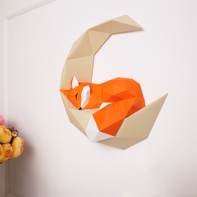 Pu&ograve; includere: Una volpe di cartapesta che dorme su una luna crescente. La volpe &egrave; arancione e bianca, e la luna &egrave; beige. La volpe e la luna sono 3D e sembrano essere appese a un muro.