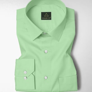 Puede incluir: Una camisa verde claro con cuello clásico y puños abotonados. La camisa tiene un bolsillo en el pecho y está doblada cuidadosamente. La marca "KOLLER CUT" es visible en una pequeña etiqueta cerca del cuello.