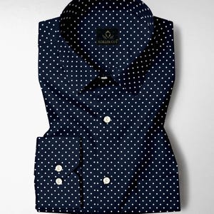 May include: A navy blue long-sleeve button-down shirt featuring a repeating white polka dot pattern. The shirt has a pointed collar, a front button placket with white buttons, and a label at the neck that reads Koller Cut in white text.