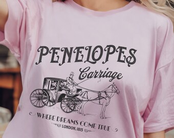May include: Pink t-shirt with a black graphic design of a horse-drawn carriage. The text on the shirt reads "PENELOPES Carriage Where Dreams Come True LONDON.1815"