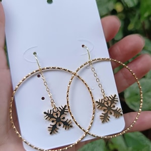 May include: A pair of gold-toned hoop earrings featuring a twisted metal texture. Each hoop is suspended from a hook and includes a delicate chain drop attached to a small, flat, four-pointed star-shaped charm with a black enamel inlay design.