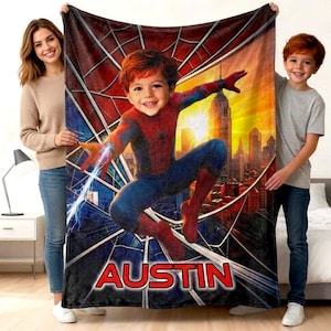Puede incluir: Una manta rectangular de forro polar con un gráfico central de un niño vestido con un traje de superhéroe rojo y azul, posado sobre un fondo de horizonte urbano y un patrón de telaraña. El nombre AUSTIN está impreso en letras rojas.