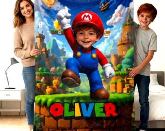 May include: A rectangular fleece blanket featuring a vibrant, colourful graphic of a child dressed as Mario from the Super Mario video game series, set against a fantasy landscape with the name OLIVER printed in bold, multi-coloured block letters.