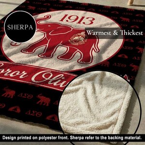 Puede incluir: Una manta sherpa negra y roja con un gr&aacute;fico grande de un elefante rojo, el a&ntilde;o 1913 y el texto "SHERPA" y "Warmest & Thickest". El dise&ntilde;o incluye siluetas de elefantes y letras griegas repetidas sobre un fondo negro con forro blanco.