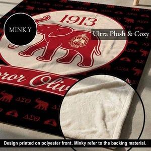 Puede incluir: Una manta minky negra y roja con un gr&aacute;fico grande de un elefante rojo, el a&ntilde;o 1913 y el texto "Delta Sigma Theta" dentro de un emblema circular. El fondo muestra un patr&oacute;n repetitivo de elefantes rojos y letras griegas sobre negro.