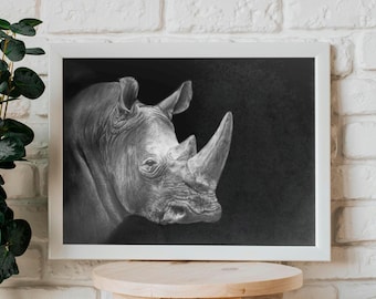 May include: Black and white framed artwork featuring a detailed pencil drawing of a rhinoceros head. The rhino's horn and textured skin are prominent. The artwork is displayed on a white brick wall, with a wooden stool in the foreground.