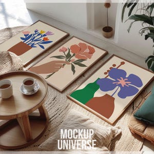 May include: Three framed floral prints with abstract designs in shades of pink, blue, green, and brown. The prints are displayed on a wall in a home setting with a wooden table and a rug.